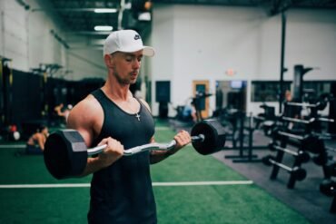 man in black tank top and white cap holding black and gray dumbbell